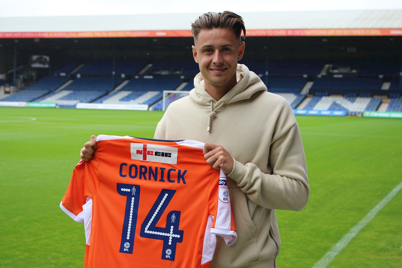 Harry Cornick holds up the number 14 shirt he will wear at Kenilworth Road