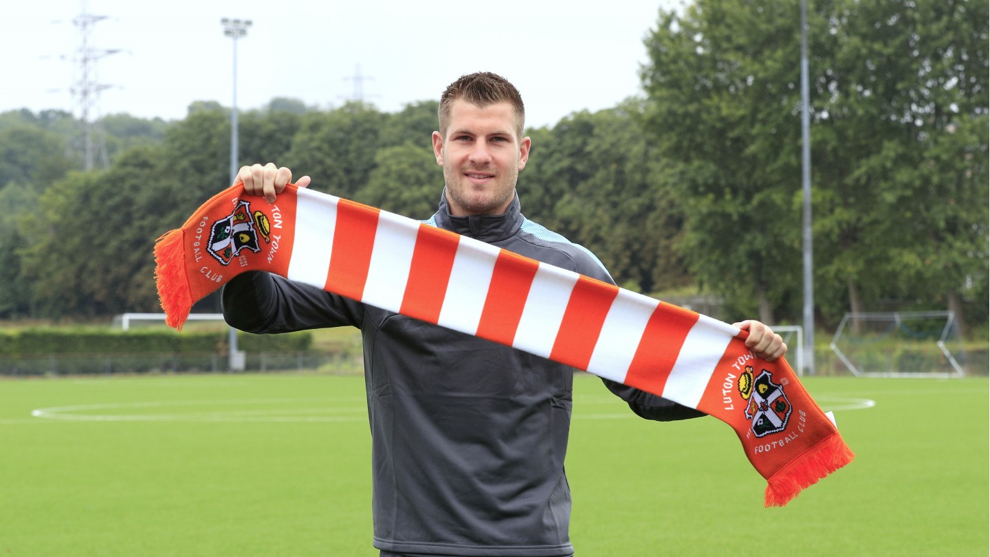 James Collins holds a Luton Town scarf aloft after agreeing to join the Hatters