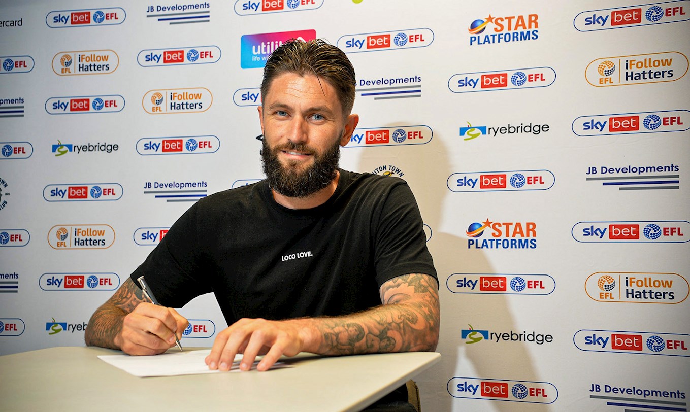 Henri Lansbury puts pen to paper on his contract in the Kenilworth Road boardroom