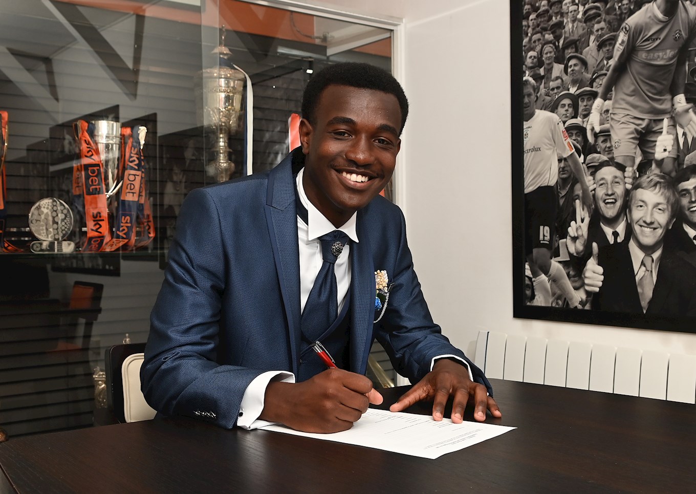 Claude Kayibanda signs his scholarship in the Trophy Room at Kenilworth Road