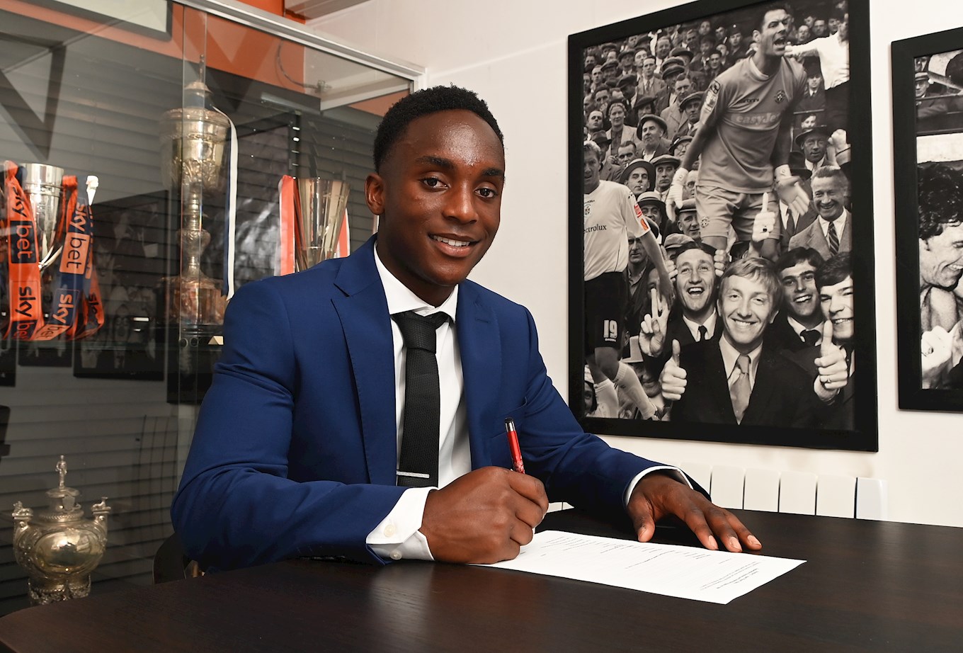 Daniel Idiakhoa signs his contract in the Trophy Room at Kenilworth Road