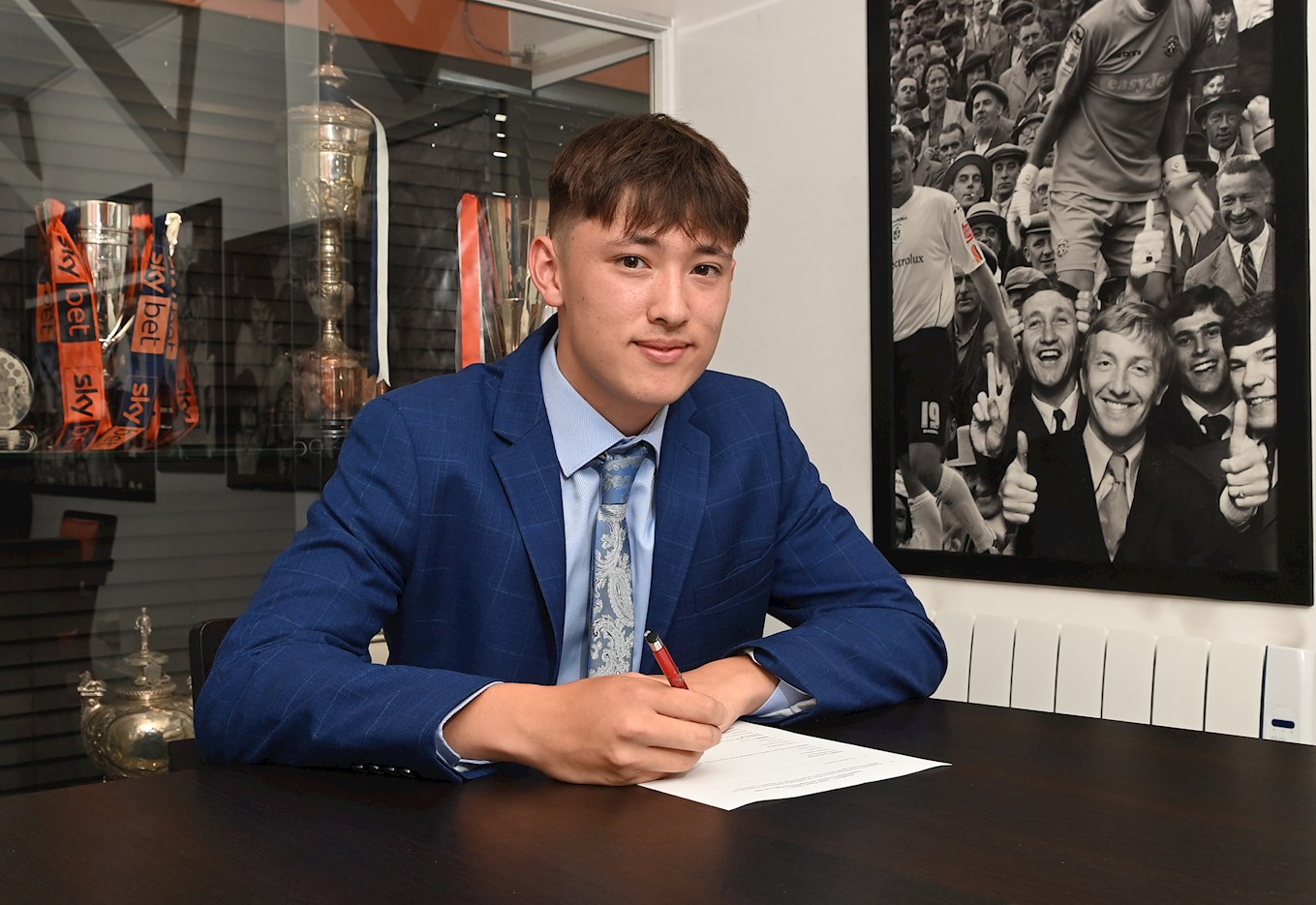 Will Houghton signs his scholarship in the Trophy Room at Kenilworth Road