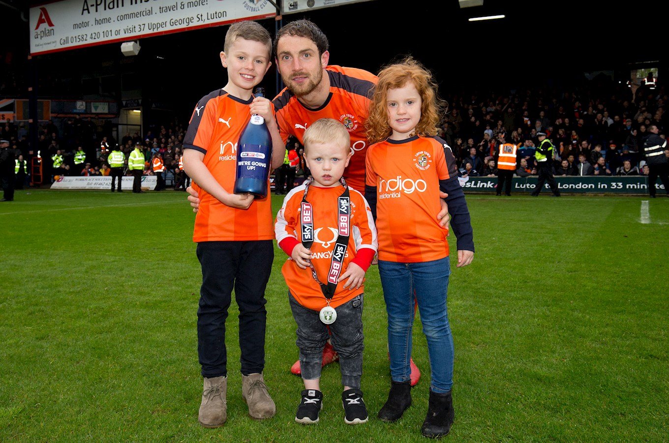 Danny Hylton celebrates promotion from League Two with his children on the pitch at Kenilworth Road