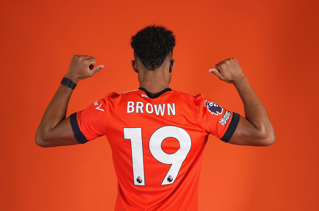 Jacob Brown pointing at the back of his shirt, which has his surname and the number 19.